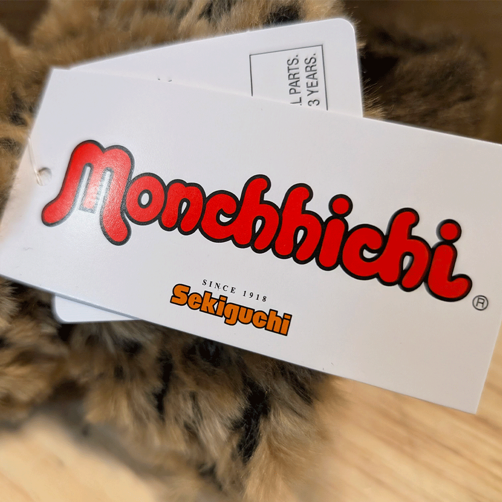 Sekiguchi Monchhichi brand tag on leopard hood and cape plush toy close-up view with clear logo text