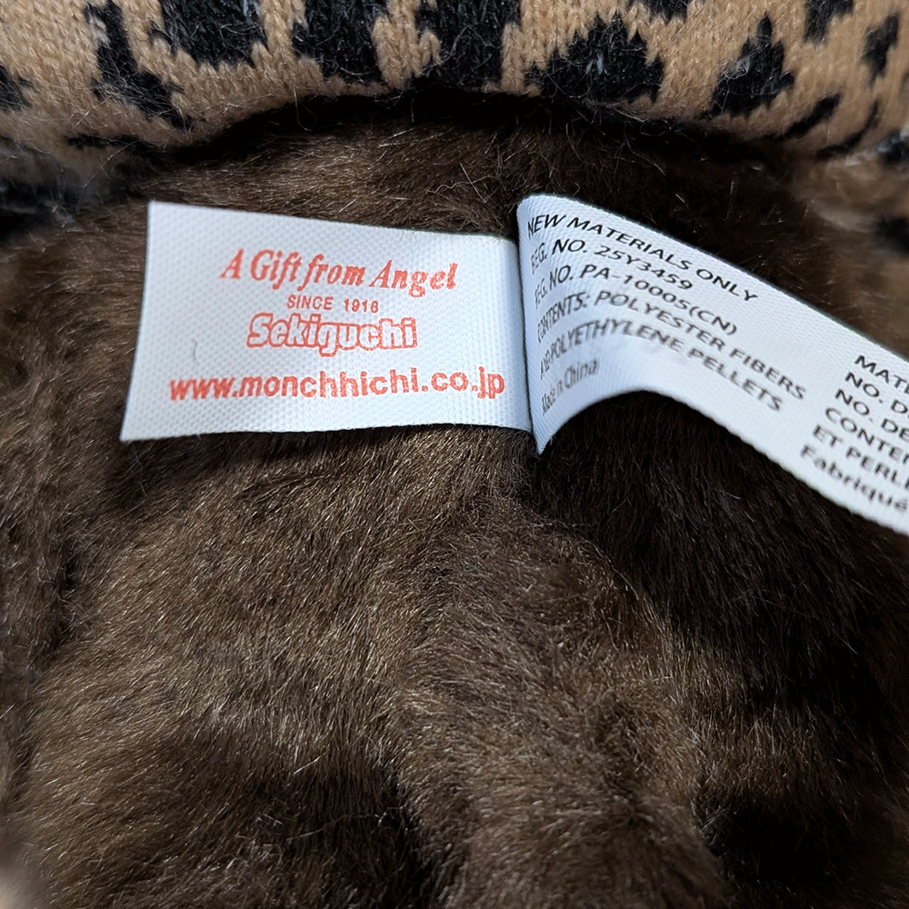 Sekiguchi Monchhichi plush tag close-up showing brand name and materials label on leopard hood and cape stuffed toy