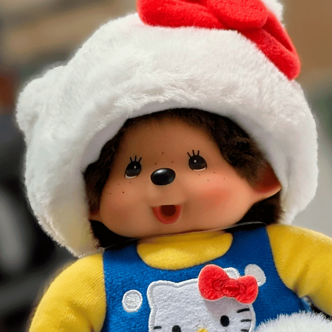 Sekiguchi Monchhichi plush doll dressed as Hello Kitty in white cat hat and blue overalls with red bow detail