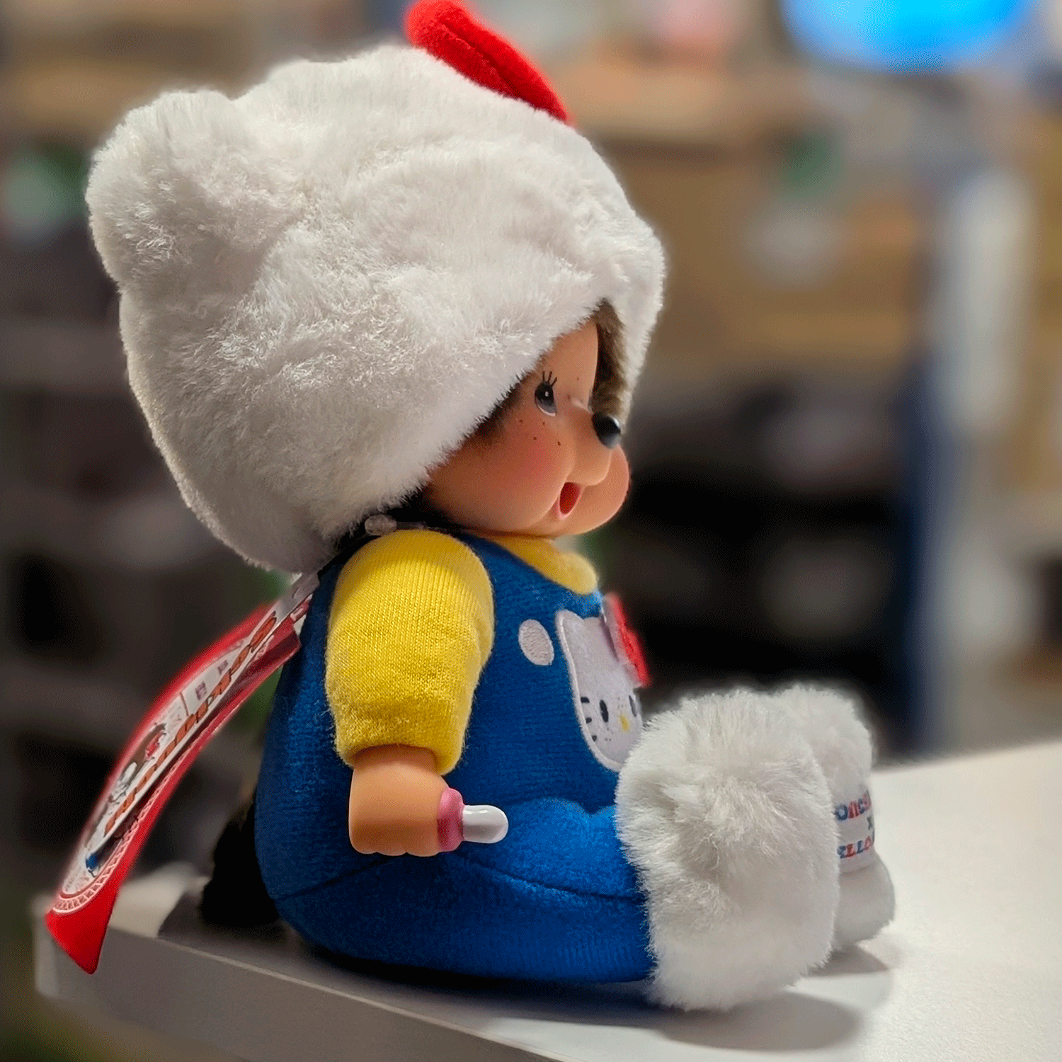 8-inch Sekiguchi Monchhichi doll dressed as white cat Hello Kitty in blue overalls sitting on white surface