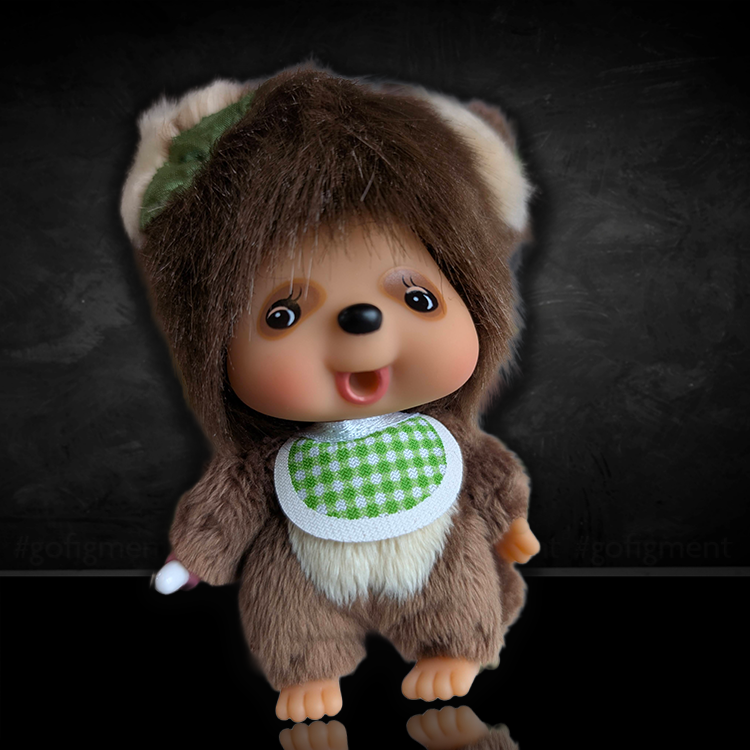 Sekiguchi Monchhichi Tanu Tanu raccoon dog plush keychain with soft fur and a green checkered bib smiling.