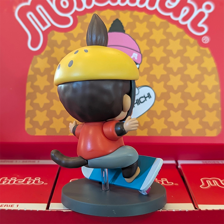 Sekiguchi Monchhichi Boy Skateboarder vinyl figure with yellow helmet on blue skateboard, displayed on gray base.