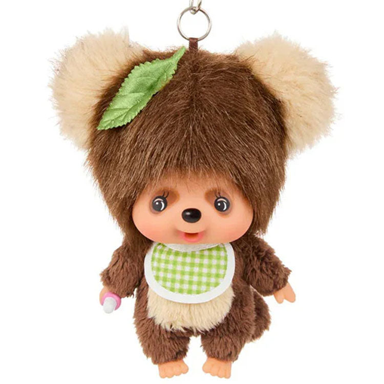 Sekiguchi Monchhichi plush keychain dressed as tanuki with green leaf and checkered bib, thumb-sucking pose.