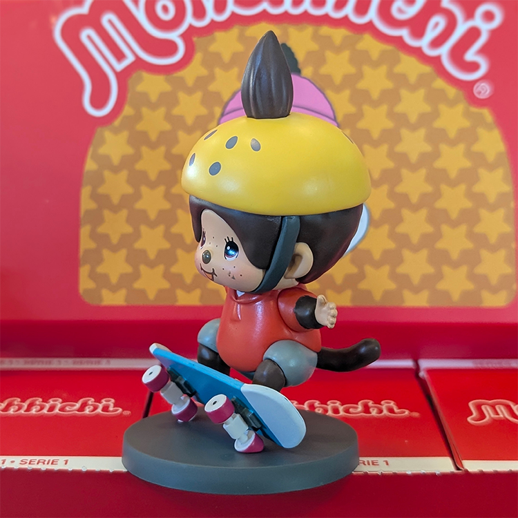 Sekiguchi Monchhichi Boy Skateboarder vinyl figure wearing yellow helmet and red shirt on blue skateboard display stand.