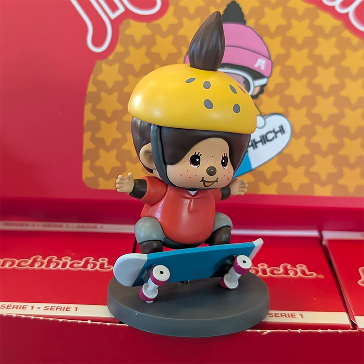 Sekiguchi Boy Monchhichi skateboarding figure wearing yellow helmet and red shirt on blue skateboard display stand