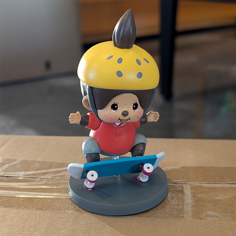 Sekiguchi Monchhichi Boy Skateboarder vinyl figure wearing yellow helmet and red shirt on blue skateboard display stand.