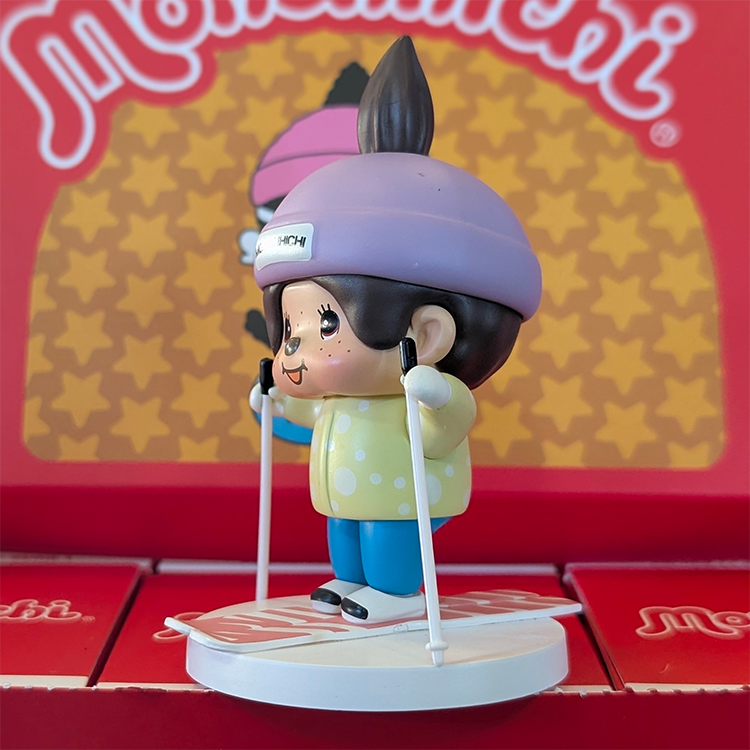Sekiguchi Boy Monchhichi skiing vinyl figure wearing purple helmet and yellow shirt on white snow base