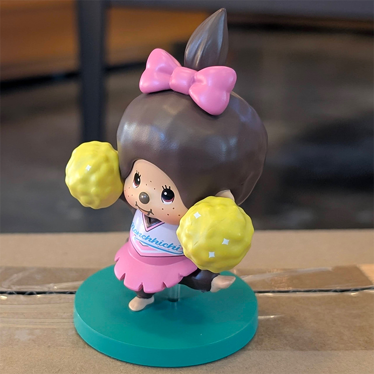 Sekiguchi Girl Monchhichi Cheerleader vinyl figure in pink outfit with yellow pom-poms on green stand
