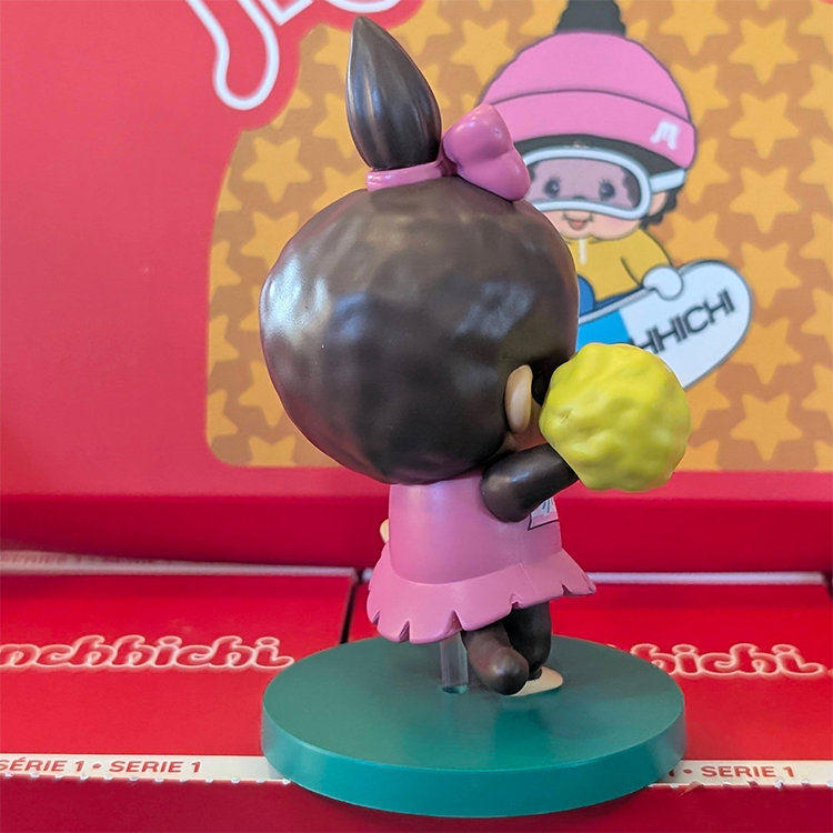 Sekiguchi Monchhichi Girl Cheerleader vinyl figure in pink outfit holding yellow pom-poms on green stand.
