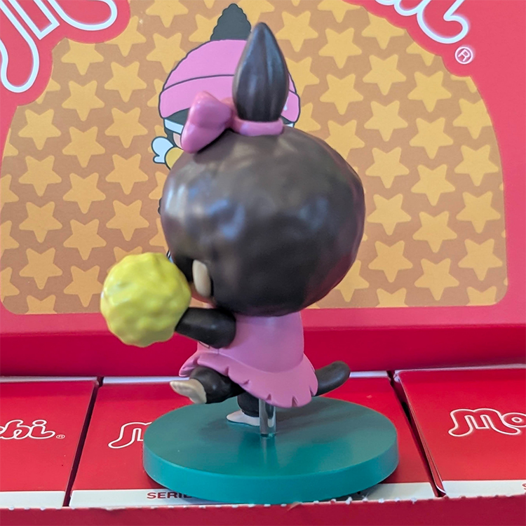 Sekiguchi Girl Monchhichi cheerleader vinyl figure in pink outfit with yellow pom-poms on green stand.