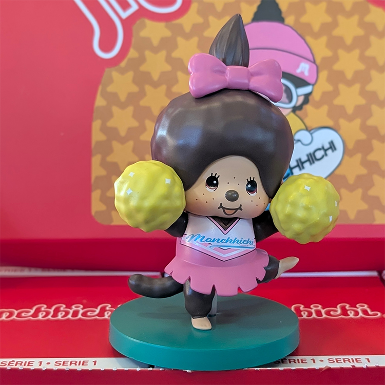 Sekiguchi Monchhichi Girl Cheerleader vinyl figure in pink outfit with yellow pom-poms on green stand.