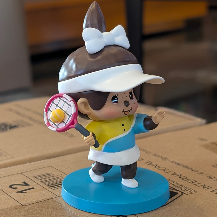 Sekiguchi Girl Monchhichi tennis player figure with white bow, visor, colorful outfit, and blue tennis court base.