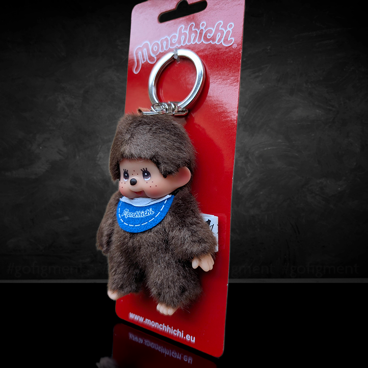 Sekiguchi Monchhichi Classic Boy plush keychain with blue bib on red card packaging, 4 inches tall.