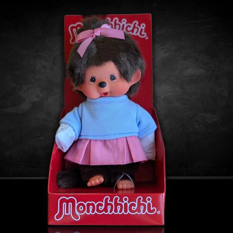 Sekiguchi Monchhichi Girl plush in pink skirt and blue shirt with thumb in mouth in branded red box.