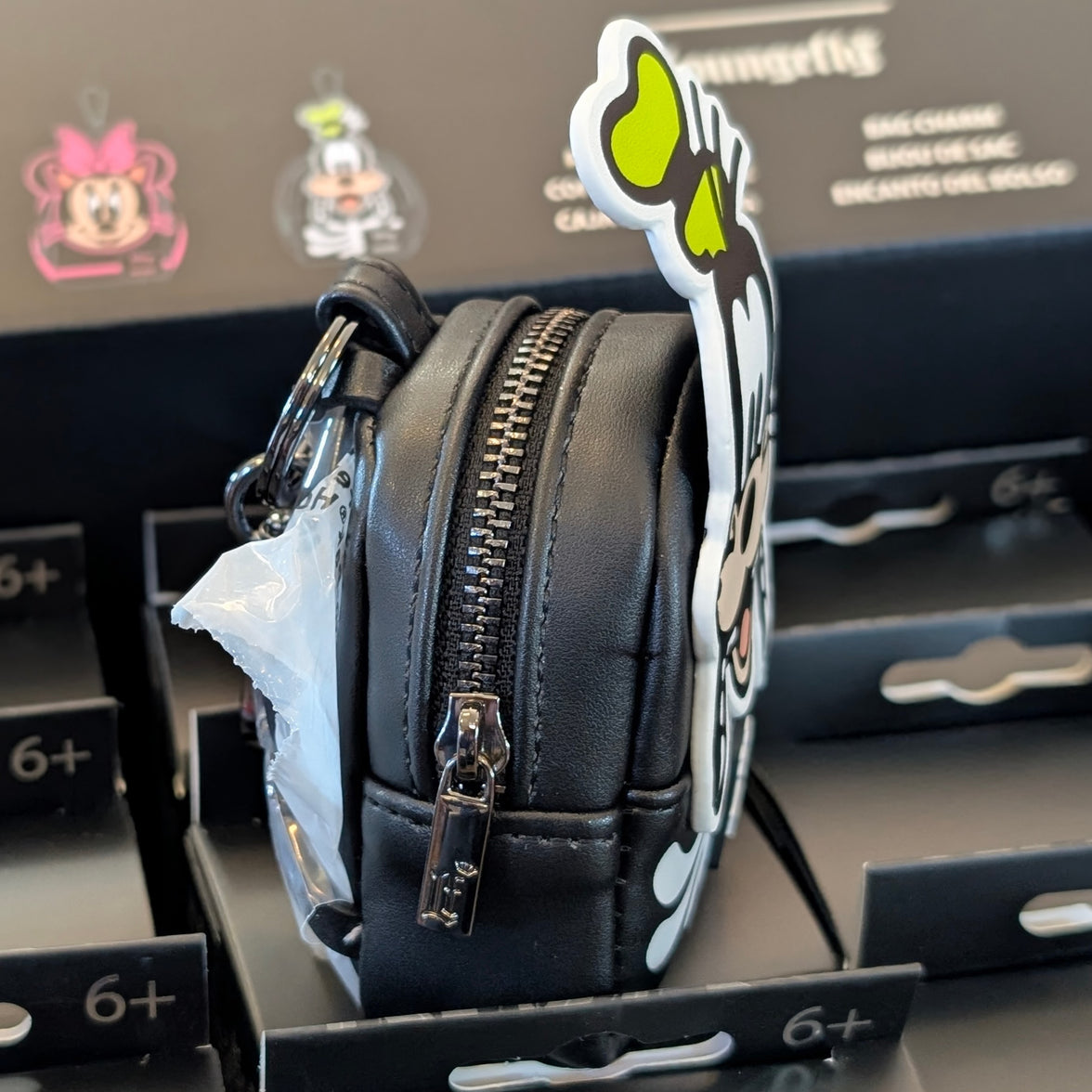Side view of black Loungefly mini backpack bag charm featuring skeleton Goofy design with zipper detail in packaging