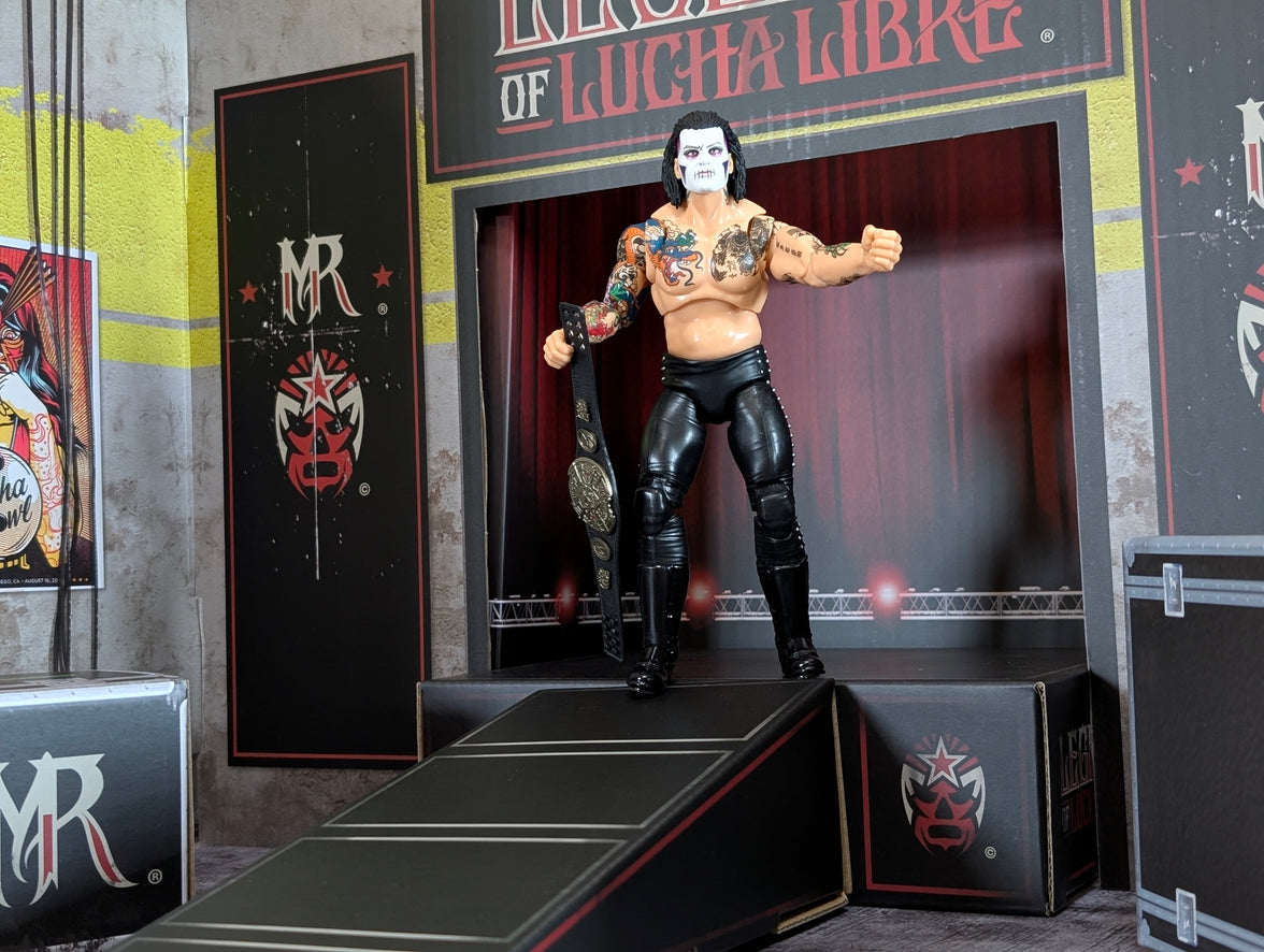 Action figure wrestler with face paint and tattoos holding a championship belt on a stage ramp with Lucha Libre branding.