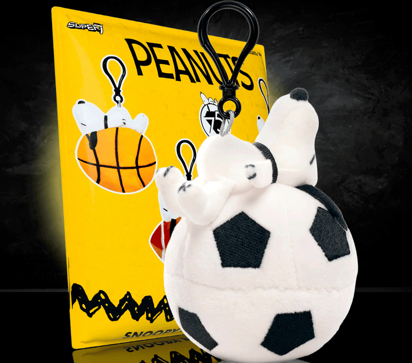 Go Figment Peanuts plush keychain featuring Snoopy on a soccer ball with black clip attached to yellow card background