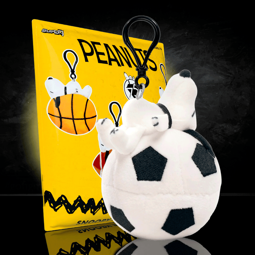Go Figment Peanuts plush keychain featuring Snoopy on a soccer ball with black clip attached to yellow card background