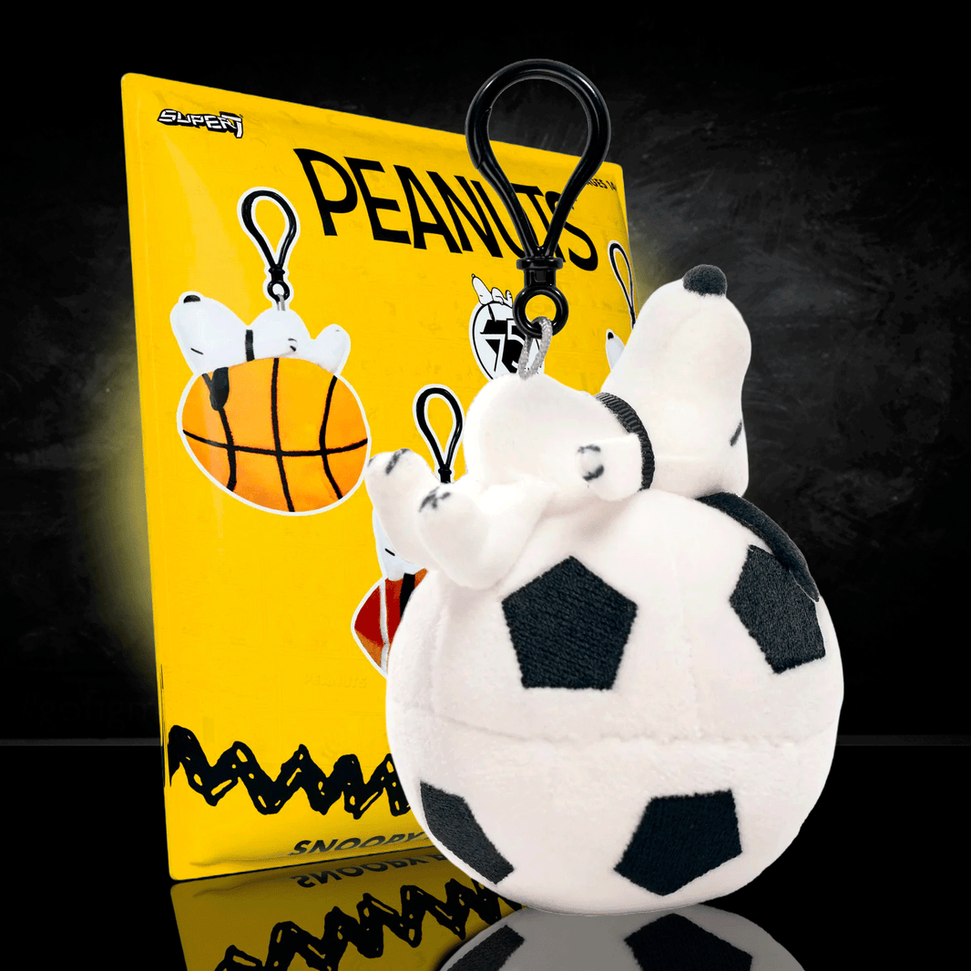 Go Figment Peanuts plush keychain featuring Snoopy on a soccer ball with black clip attached to yellow card background