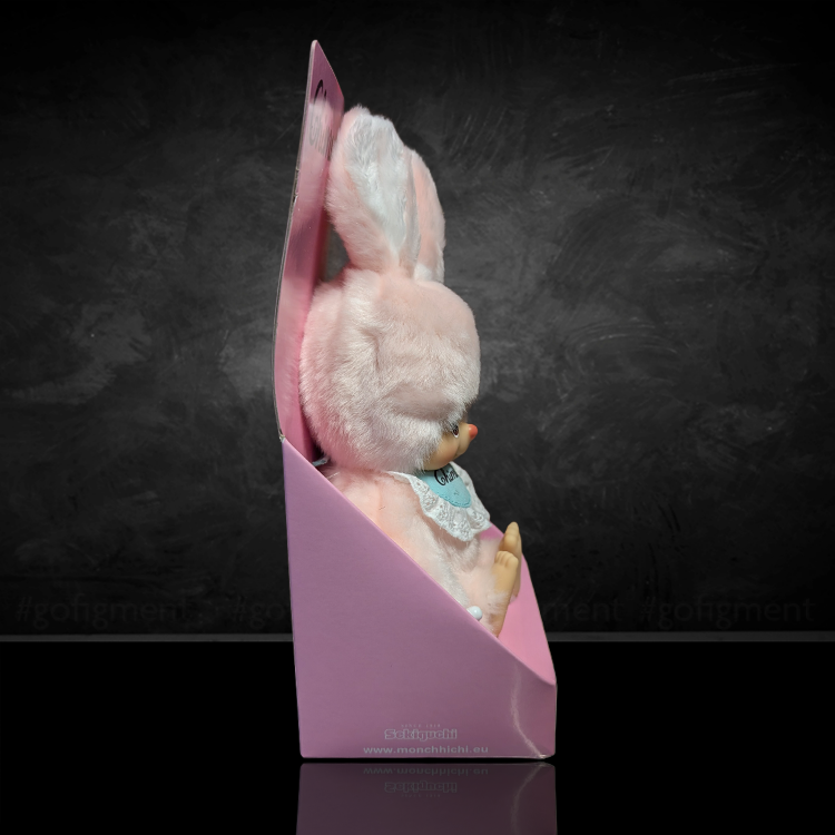 Sekiguchi Monchhichi Chimutan Bunny plush in pastel pink with blue bib displayed in pink box against dark background