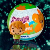 Scooby-Doo mini figure collectible by UCC with colorful mystery ball packaging in background on reflective surface