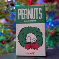 Super7 Peanuts Holiday Blind Box featuring Snoopy inside green wreath with red bow and colorful festive lights background