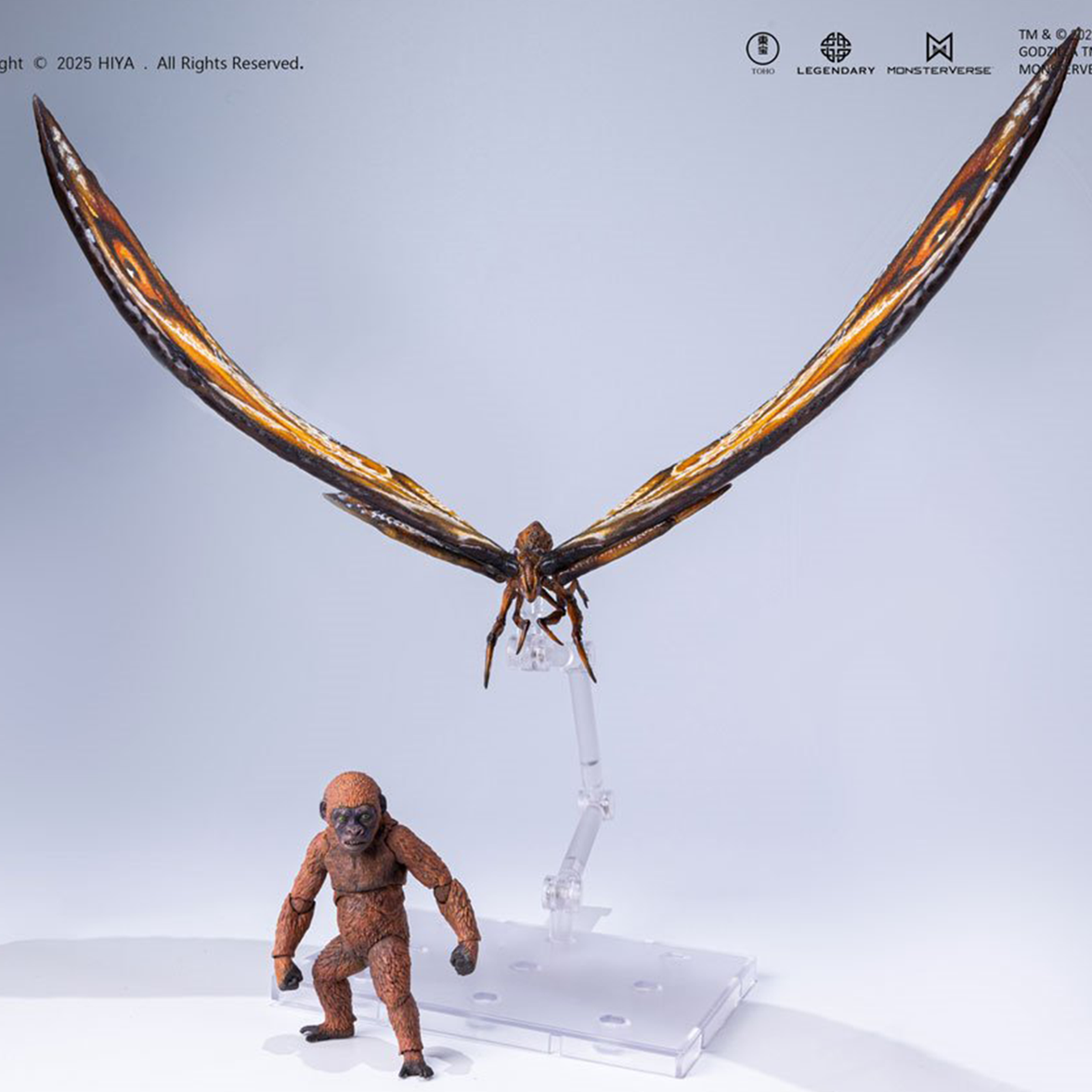 Detailed winged moth figure with outstretched wings mounted on clear stand beside articulated ape figure on white surface