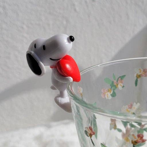 K-Wonderland Peanuts Snoopy cup figure clutching a red heart perched on a floral glass rim in playful pose